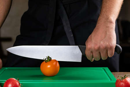 chef holds a knife for cutting vegetables on a plastic board