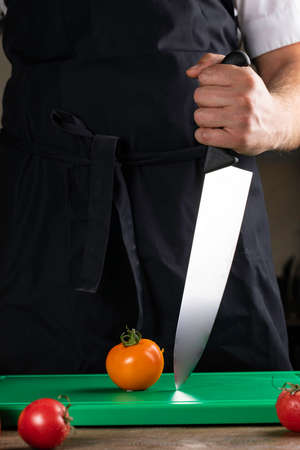 chef holds a knife for cutting vegetables on a plastic boardの写真素材