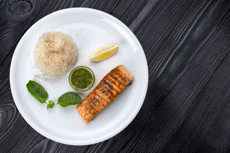 Grilled salmon with rice on a white plate and black backgroundの写真素材