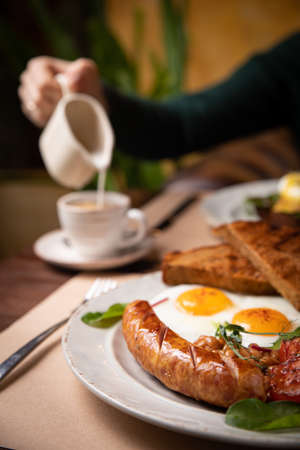 Full English breakfast - fried egg, baked beans, bacon, sausages on a dark rusty background, toasts.