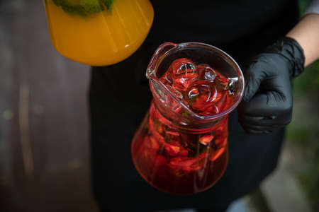 Waiter brings jars of fresh fruit cocktails to customer. Orange and strawberry cold drink with mint...