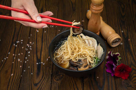 Thai spicy soup with pasta, mushrooms and meat in a dark plate on a wooden backgroundの写真素材