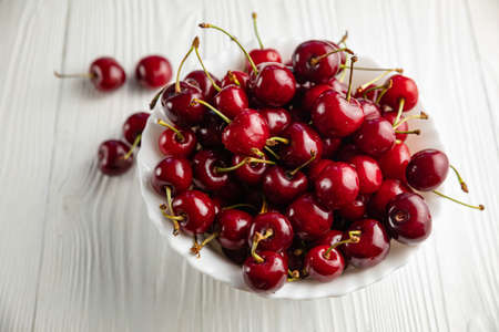 ripe cherries in a white plate on a white wooden background. Vegetarian concept, food.