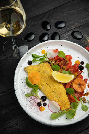 breaded sea fish fillet. With vegetable garnish. On a dark wooden table.