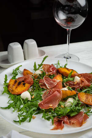 Jamon with arugula and peach on a white plate. On a white wooden table.の写真素材