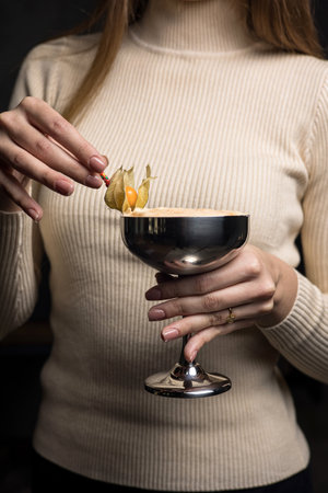 Female hand holding a glass of cocktail decorated with physalis flower.の写真素材