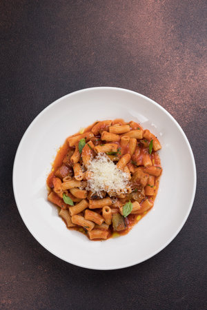 Penne pasta with tomato sauce, parmesan cheese and basil in white plate on dark brown backgroundの写真素材