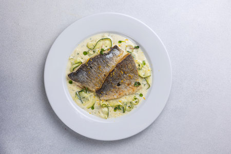 Fried fish with zucchini and cream sauce on white plateの写真素材