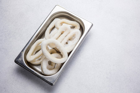 Raw squid rings in stainless steel box on white background, top viewの写真素材