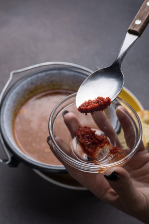 Hands holding spoon with chili sauce in a pot on dark backgroundの写真素材