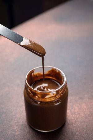 Pouring chocolate syrup into a glass jar with spoon on wooden tableの写真素材