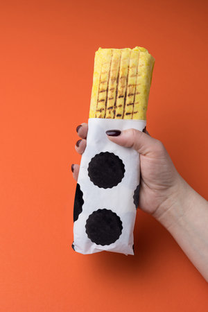 Female hand holding a tortilla wrap on orange background. Top view.