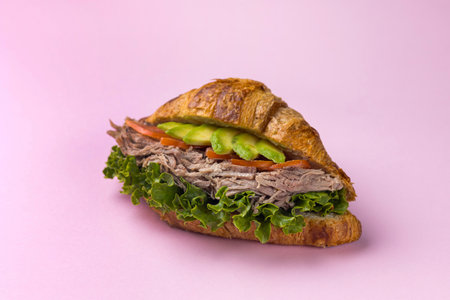 Croissant sandwich with ham and vegetables on a pink background.の写真素材