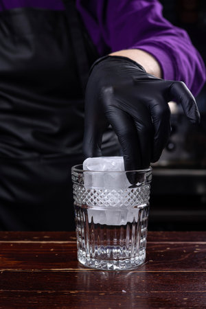Close-up of bartender hands in black gloves pouring ice into glassの写真素材
