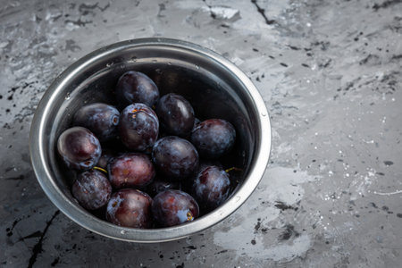 Ripe plums in a metal colander on a gray backgroundの写真素材