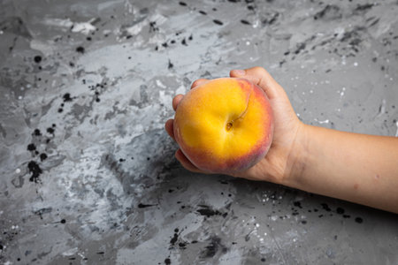 Woman's hand holding a ripe peach on a gray concrete background.の写真素材