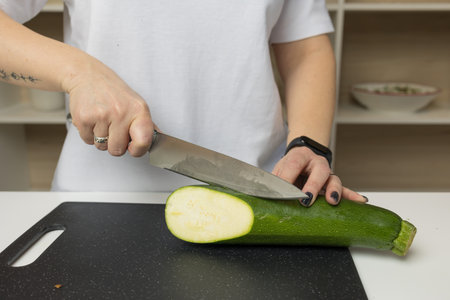 A woman cuts a zucchini on a cutting board with a knifeの写真素材