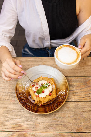 Woman holding a cup of cappuccino and a piece of cake on a wooden tableの写真素材