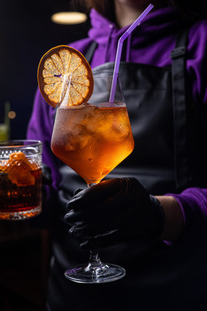Bartender in black gloves holding a glass of cocktail with orangeの写真素材