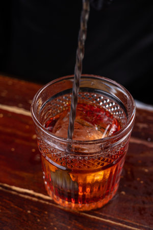 Bartender pouring whiskey into a glass with ice cubes, close upの写真素材
