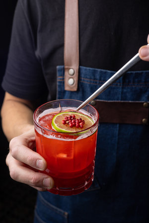 Barman is holding a glass of red cocktail with lime and pomegranateの写真素材