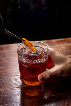 Bartender decorating a cocktail with orange peel in a glass