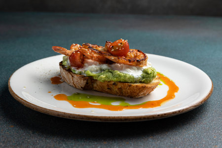 Toast with avocado, fried shrimp and tomato on a white plateの写真素材