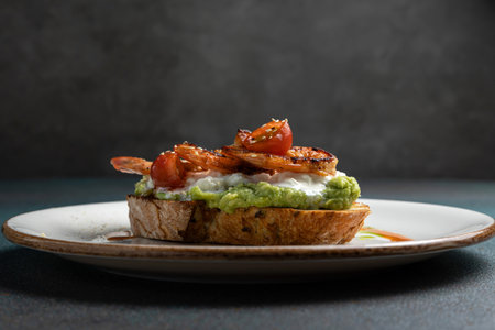 sandwich with avocado and tomatoes on a white plate on a dark backgroundの写真素材