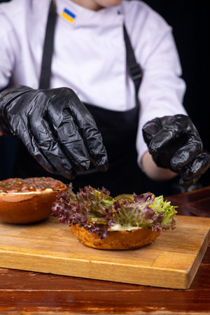 Chef in black gloves preparing a hamburger on a wooden boardの写真素材