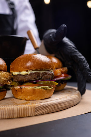 Chef in black gloves with hamburgers on a wooden boardの写真素材