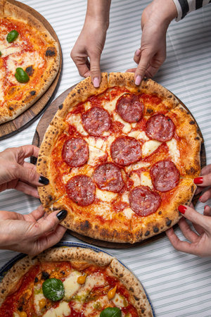 Group of people taking slices of pepperoni pizza from a wooden plateの写真素材