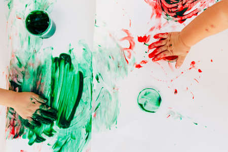 2-3 years old boys paint with hands on white paper, with bare hands, they using green, red and blue colour on white canvas paper.の写真素材