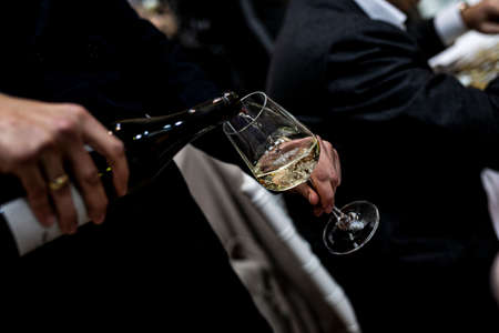 Waiter is pouring white wine into wine glass. no face shown.の写真素材