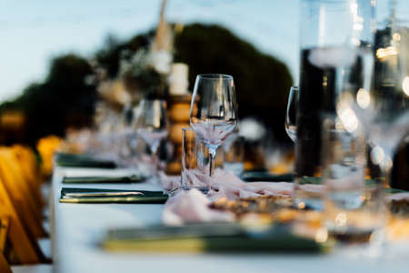 Luxury table settings for fine dining with and glassware, pouring wine to glass. Beautiful blurred background. Preparation for holiday wedding. Fancy luxury restaurant.の写真素材