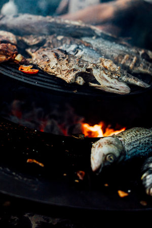 delicious grilled meat and fish with vegetables and fresh herbs  on barbecue grill with smoke and flames at outside social event natural soft light. 2024 content.の写真素材