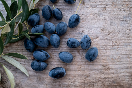 Freshly harvested black olives scattered on a rustic wooden background, with an olive branch adding a natural touch. A perfect representation of Mediterranean agriculture and organic farming.の写真素材