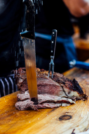 Juicy smoked beef brisket being freshly sliced on a wooden cutting board during a barbecue event....