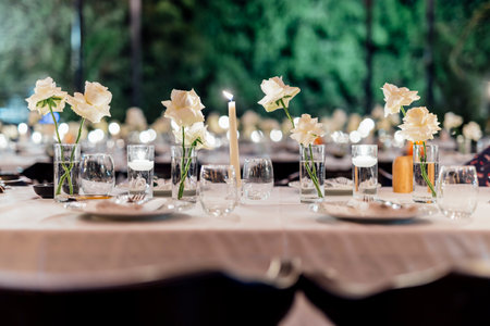 Romantically set dinner table with wine glasses and floral centerpiece, perfect for a wedding, elegant party, or outdoor evening celebration. Warm lights and soft bokeh create an intimate and luxurious atmosphere.の写真素材