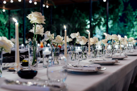 Romantically set dinner table with wine glasses and floral centerpiece, perfect for a wedding, elegant party, or outdoor evening celebration. Warm lights and soft bokeh create an intimate and luxurious atmosphere.の写真素材