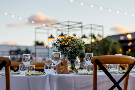 Romantically set dinner table with wine glasses and floral centerpiece, perfect for a wedding, elegant party, or outdoor evening celebration. Warm lights and soft bokeh create an intimate and luxurious atmosphere.の写真素材
