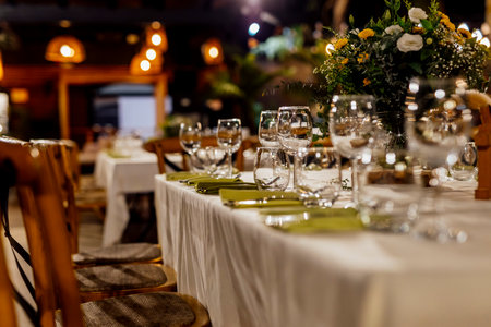 Romantically set dinner table with wine glasses and floral centerpiece, perfect for a wedding, elegant party, or outdoor evening celebration. Warm lights and soft bokeh create an intimate and luxurious atmosphere.の写真素材