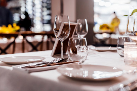 Romantically set dinner table with wine glasses and floral centerpiece, perfect for a wedding, elegant party, or outdoor evening celebration. Warm lights and soft bokeh create an intimate and luxurious atmosphere.の写真素材