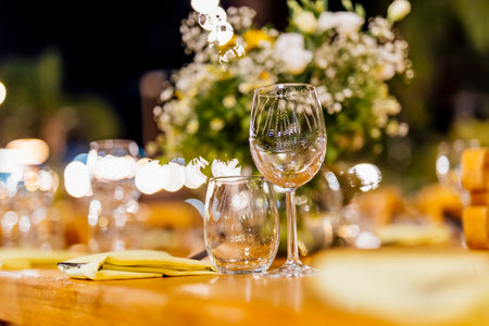Romantically set dinner table with wine glasses and floral centerpiece, perfect for a wedding, elegant party, or outdoor evening celebration. Warm lights and soft bokeh create an intimate and luxurious atmosphere.の写真素材