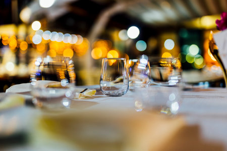Romantically set dinner table with wine glasses and floral centerpiece, perfect for a wedding, elegant party, or outdoor evening celebration. Warm lights and soft bokeh create an intimate and luxurious atmosphere.の写真素材