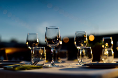 Romantically set dinner table with wine glasses and floral centerpiece, perfect for a wedding, elegant party, or outdoor evening celebration. Warm lights and soft bokeh create an intimate and luxurious atmosphere.の写真素材