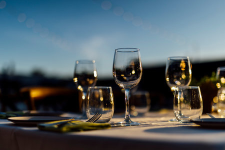 Romantically set dinner table with wine glasses and floral centerpiece, perfect for a wedding, elegant party, or outdoor evening celebration. Warm lights and soft bokeh create an intimate and luxurious atmosphere.の写真素材
