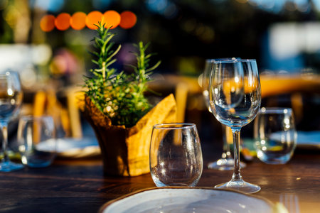 Romantically set dinner table with wine glasses and floral centerpiece, perfect for a wedding, elegant party, or outdoor evening celebration. Warm lights and soft bokeh create an intimate and luxurious atmosphere.の写真素材