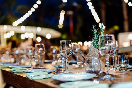 Romantically set dinner table with wine glasses and floral centerpiece, perfect for a wedding, elegant party, or outdoor evening celebration. Warm lights and soft bokeh create an intimate and luxurious atmosphere.の写真素材