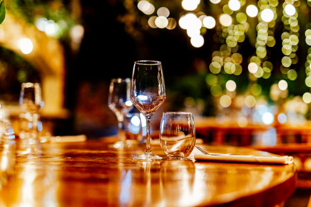 Elegant Christmas table setting with wine glasses and warm golden bokeh lights in a cozy restaurant atmosphere."の写真素材