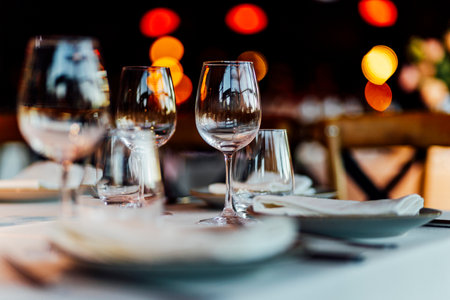 Elegant Christmas table setting with wine glasses and warm golden bokeh lights in a cozy restaurant atmosphere."の写真素材